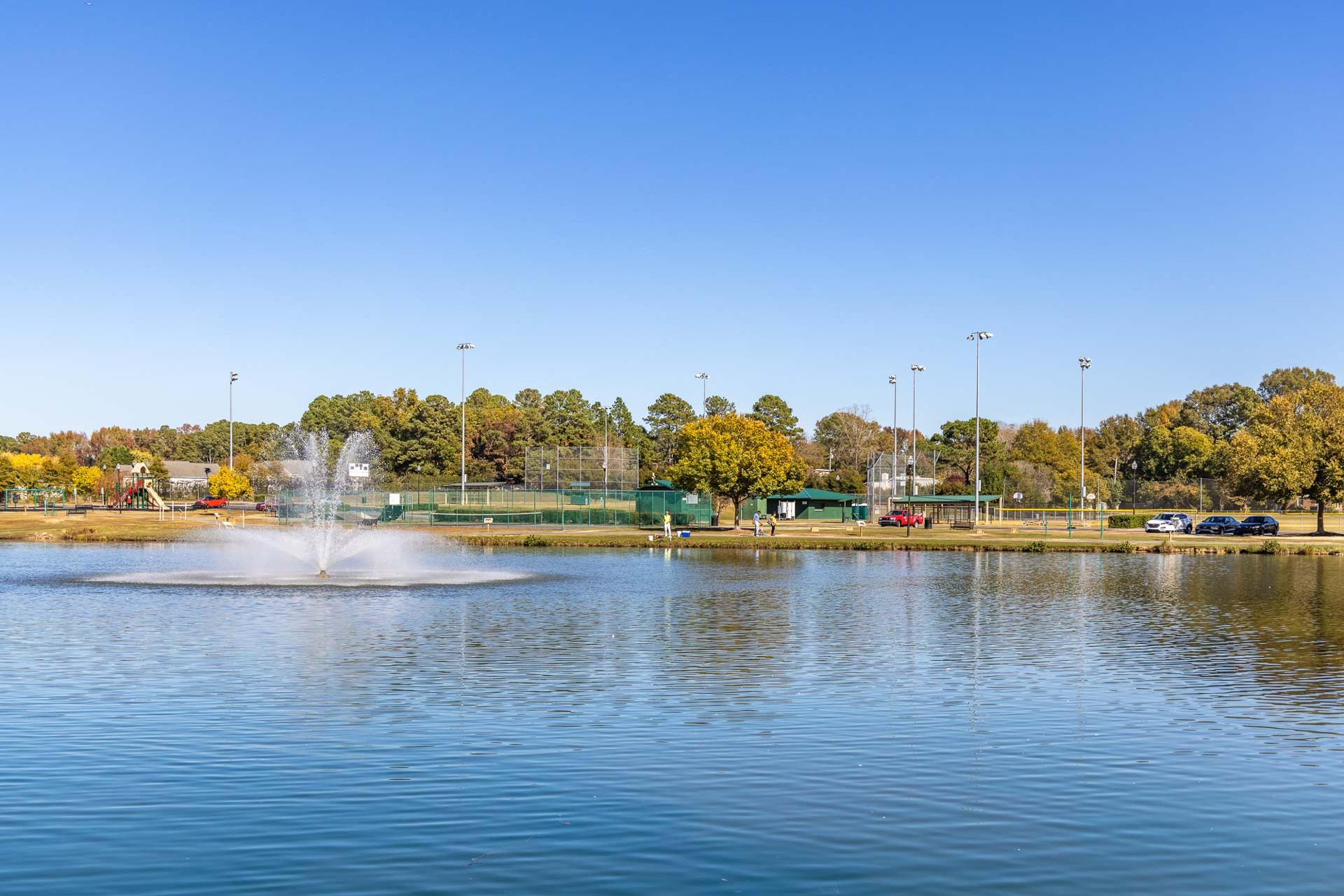 Serene pond with fountain and tennis courts at Tobacco Road in Angier, North Carolina amid autumn trees