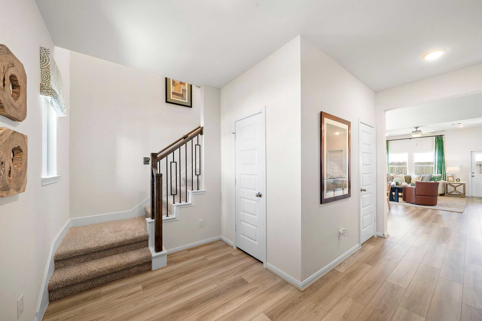 Spacious modern hallway with carpeted staircase, abstract wood wall art, and open living area in River Ranch Meadows, Dayton Texas home