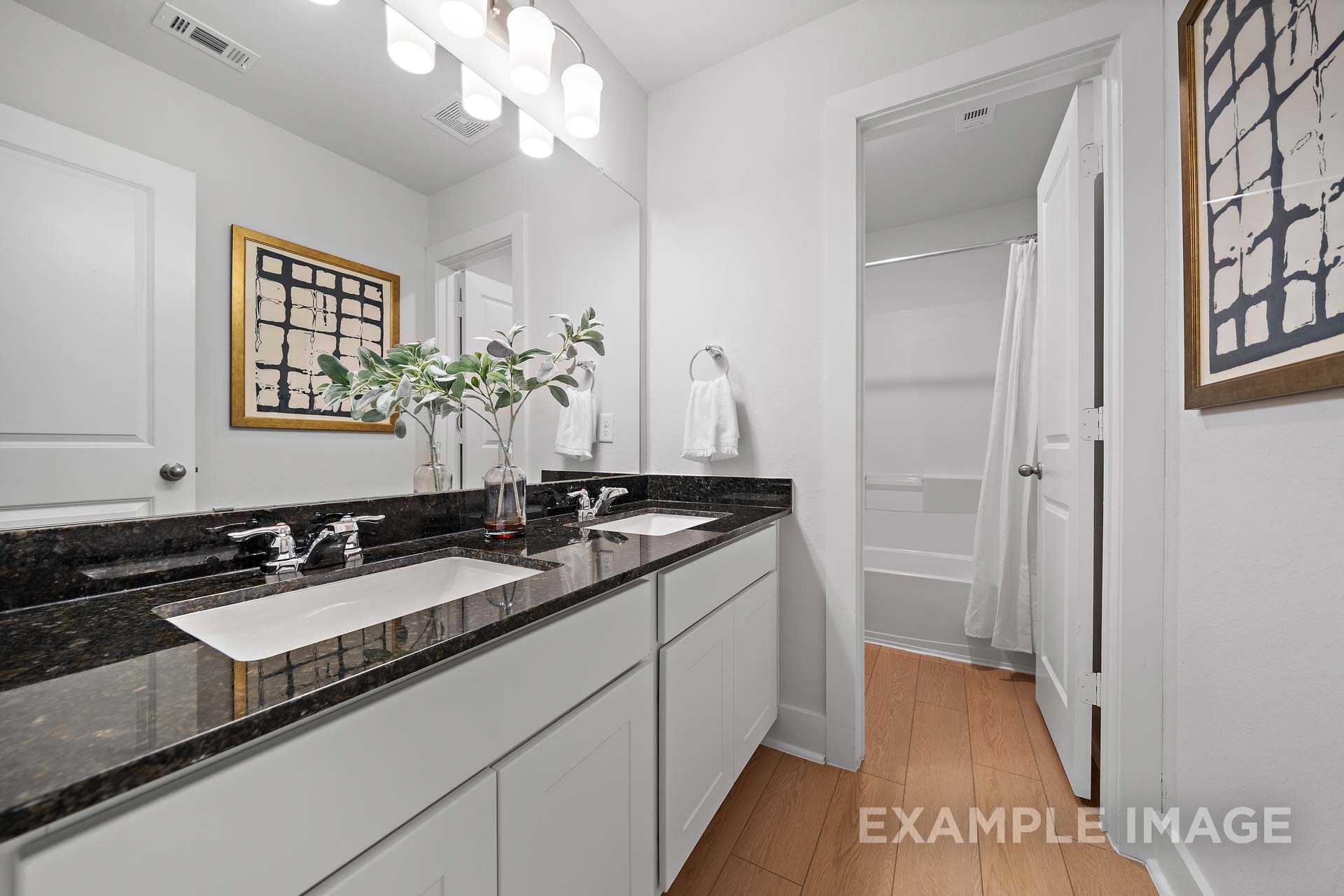 Modern master bathroom in The Rose B with double granite vanity, white cabinetry, abstract wall art, and open shower