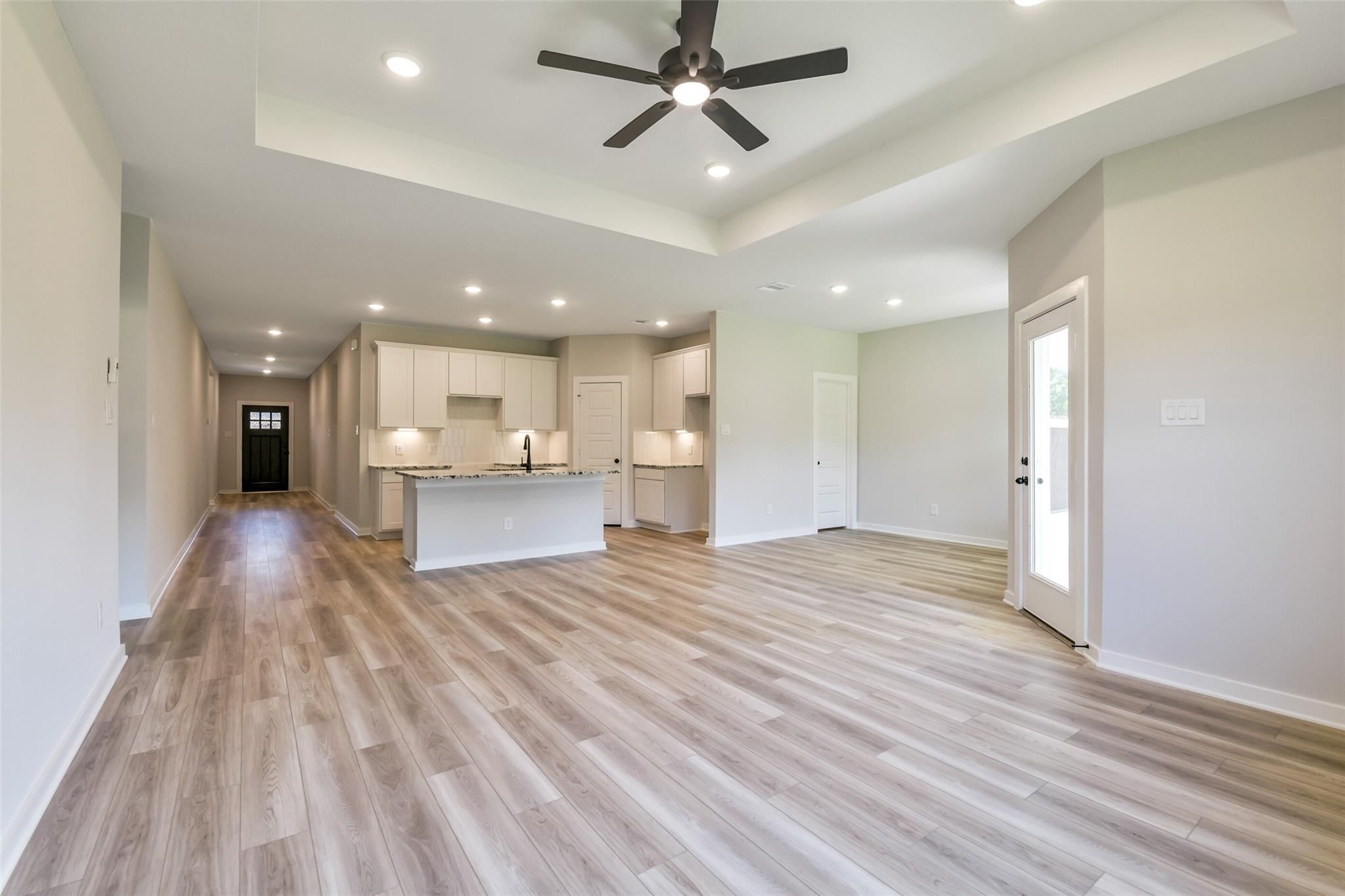 Open-concept kitchen and living area with white cabinets, large island, ceiling fans, and hardwood floors in 4-bedroom Davidson Homes The Daphne H, Crosby, Texas
