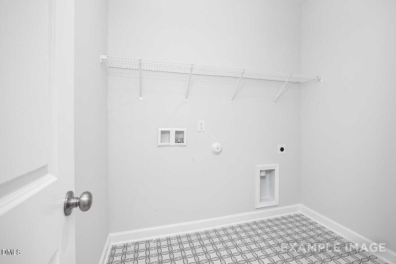Modern laundry room with white hanging rod, washer dryer hookups, checkered tile floor in The Daphne C, Lillington, NC