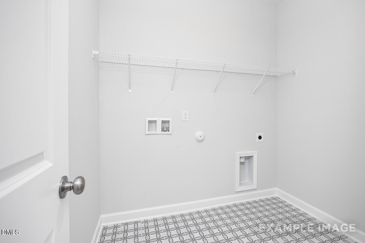 Modern laundry room with white walls, hanging rods, utility sink, and checkered tile floor in The Daphne C 4-bedroom home, Zebulon, NC