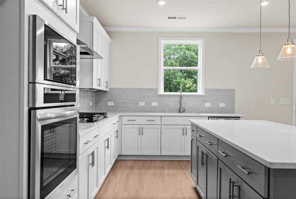 Modern kitchen with white cabinets, stainless steel appliances, gray backsplash, and quartz island in Davidson Homes The Hickory B at Wehunt Meadows, Hoschton