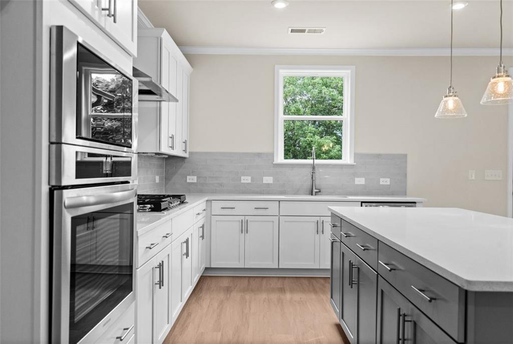 Modern kitchen with white cabinets, stainless steel appliances, gray backsplash, and quartz island in Davidson Homes The Hickory B at Wehunt Meadows, Hoschton