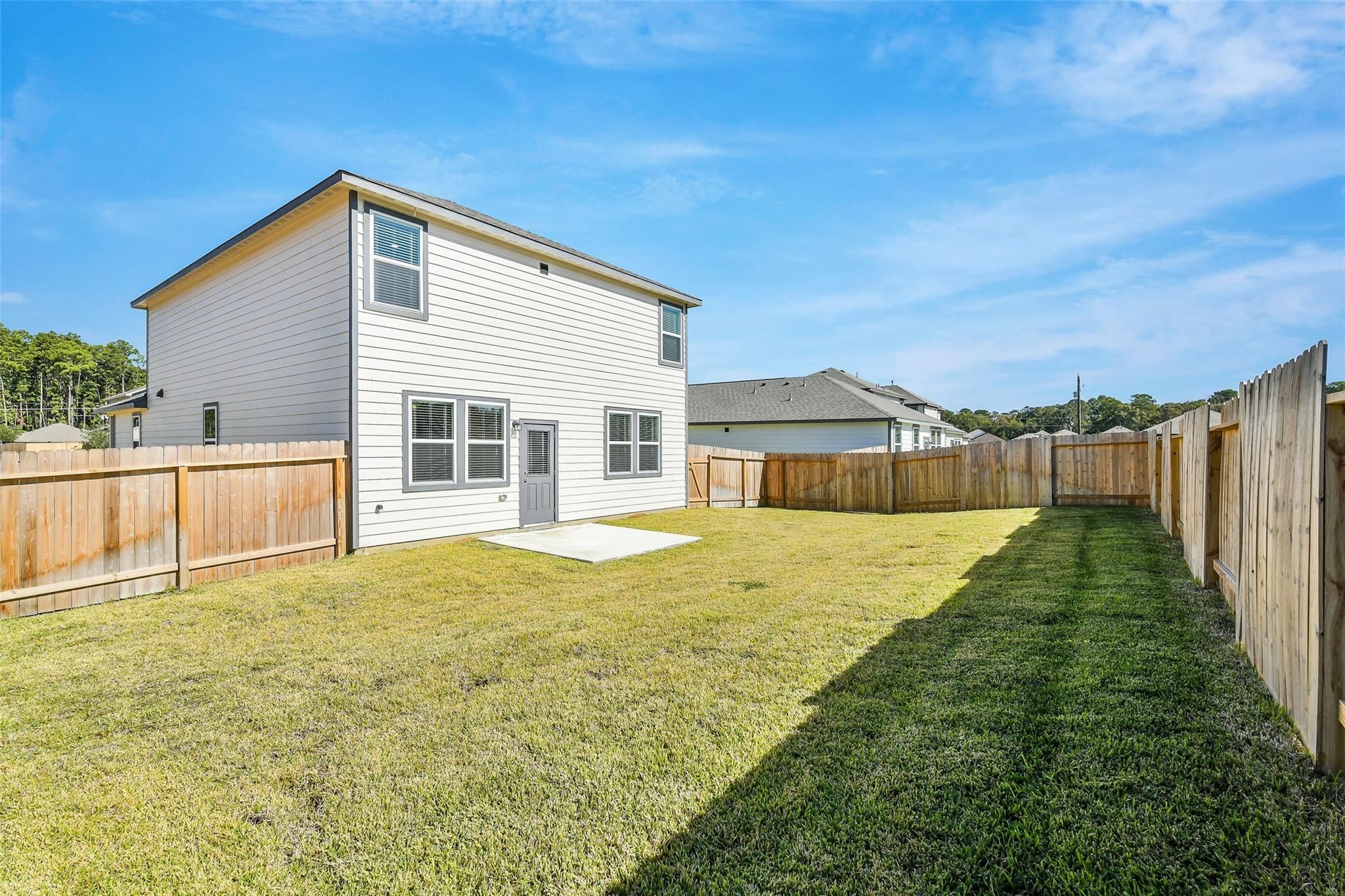 Backyard of two-story San Marcos E home with covered patio, wooden fence, lush green lawn in Liberty Estates, Cleveland, Texas