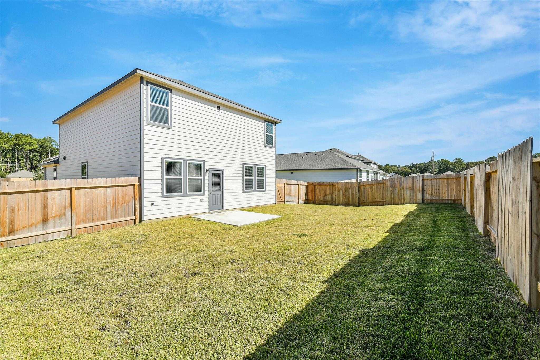 Backyard of two-story San Marcos E home with covered patio, wooden fence, lush green lawn in Liberty Estates, Cleveland, Texas