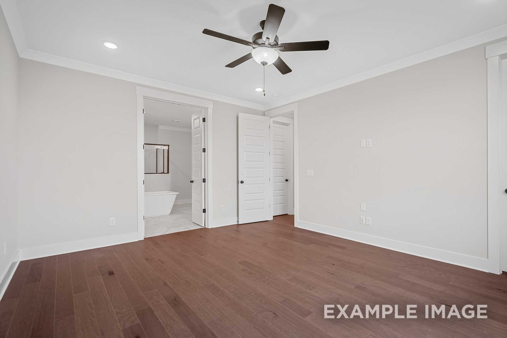Spacious master bedroom in The Hathaway with hardwood floors, ceiling fan, and en-suite bath featuring freestanding tub