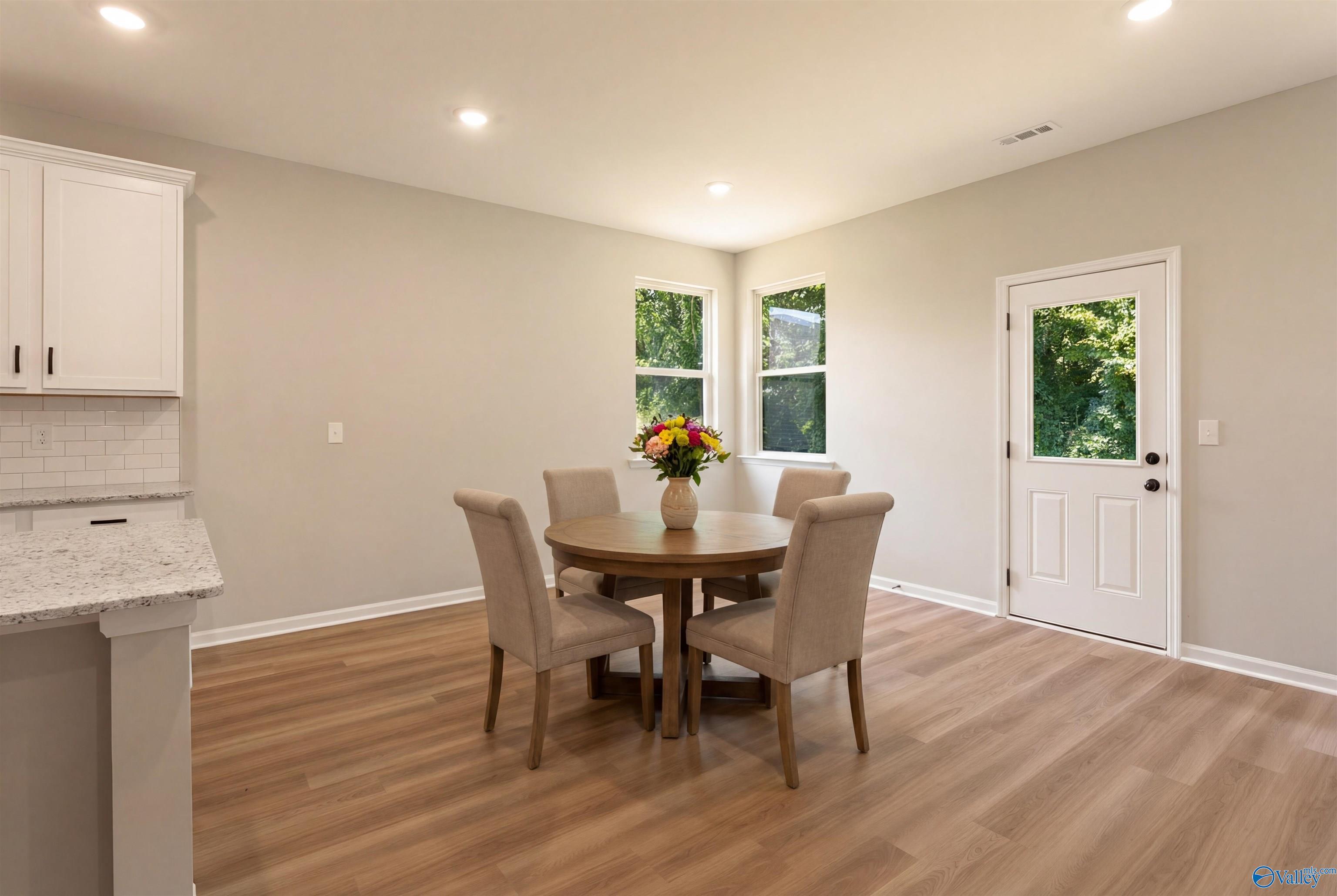 Elegant dining area with round wood table, upholstered chairs, and floral vase in open-concept home, The Phoenix by Davidson Homes, Hazel Green AL