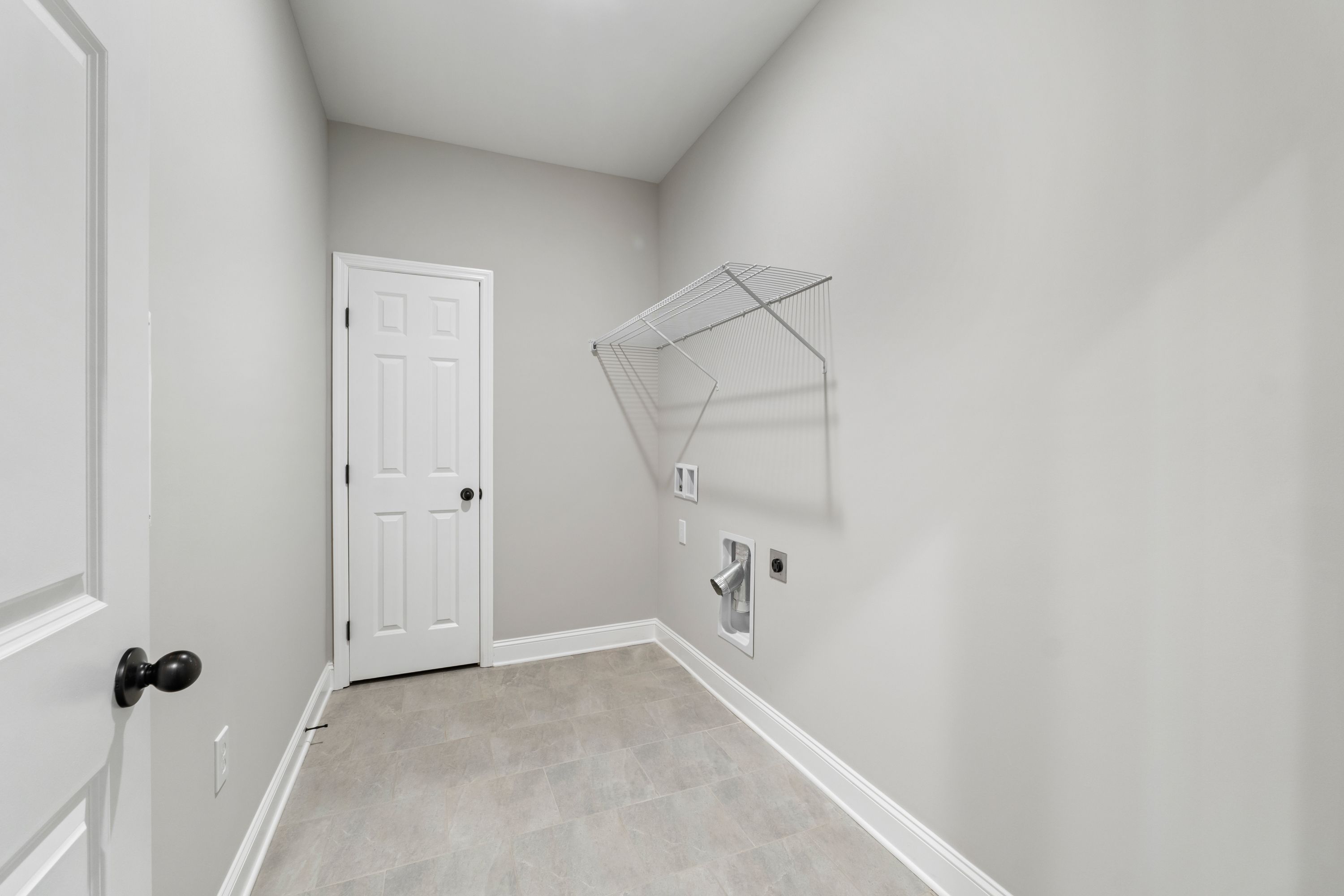 Spacious laundry room in The Valencia featuring gray walls, white door, wire shelving, and washer-dryer hookups
