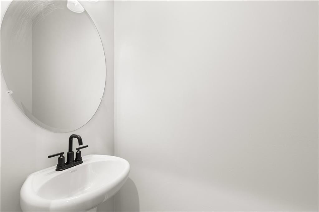 Modern powder room featuring white pedestal sink, black faucet, and round mirror in Davidson Homes The Cary A, Winder, Georgia