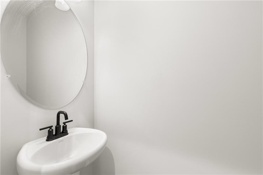 Modern powder room featuring white pedestal sink, black faucet, and round mirror in Davidson Homes The Cary A, Winder, Georgia