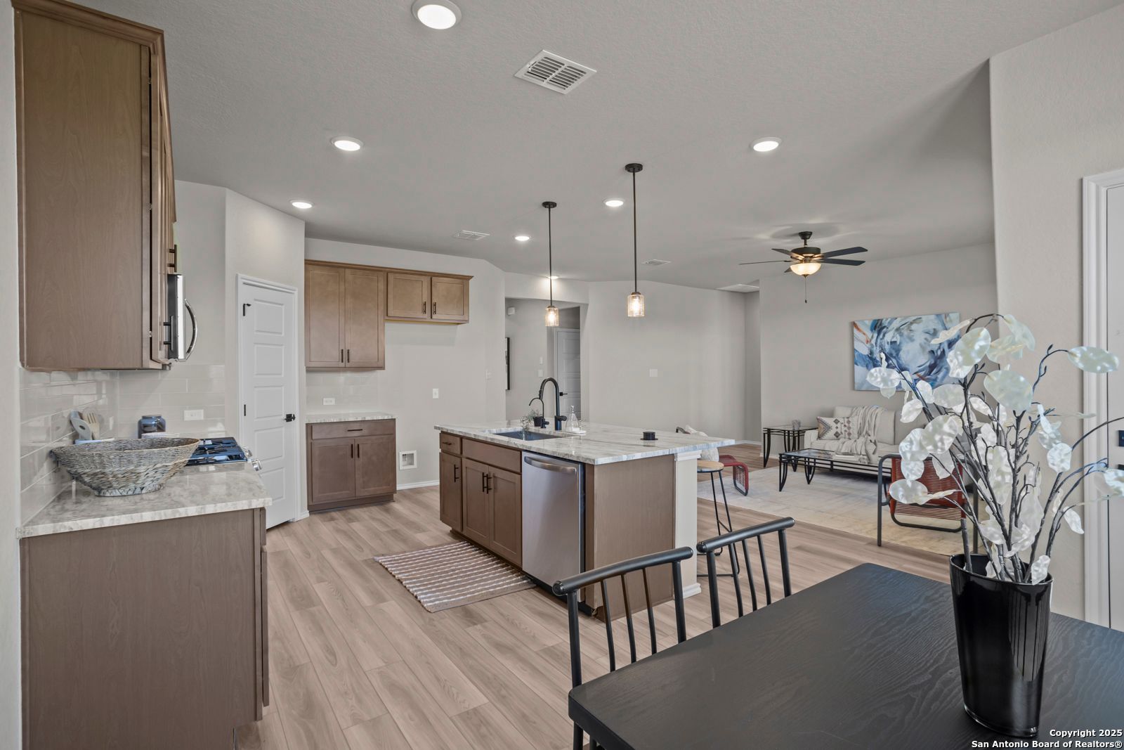 Modern open-concept kitchen with brown cabinets, large island sink, and dining area in Davidson Homes Asheville H, Converse, Texas