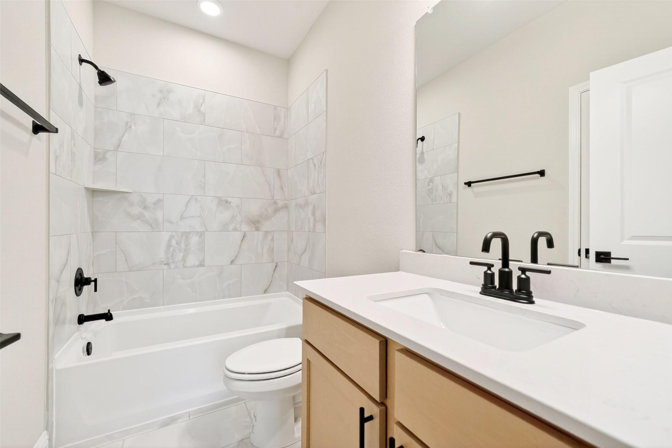 Modern bathroom with marble-look tile tub surround and vanity in The Holly C floor plan at Parks at Foster Crossing, Anna.