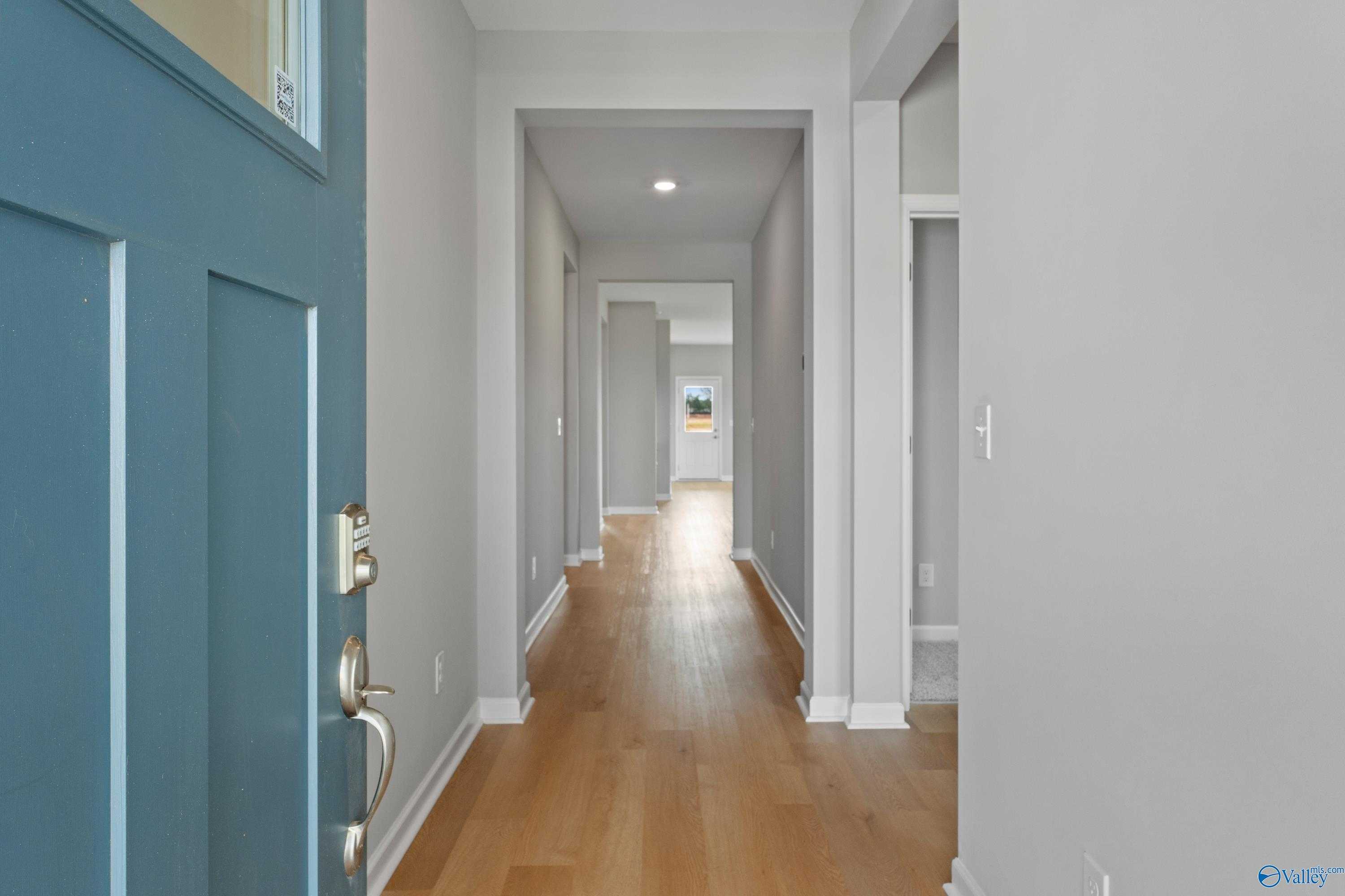 Bright entry hallway with open teal door, light hardwood floors, and modern rooms in Evermore Homes The Aurora, Harvest, Alabama