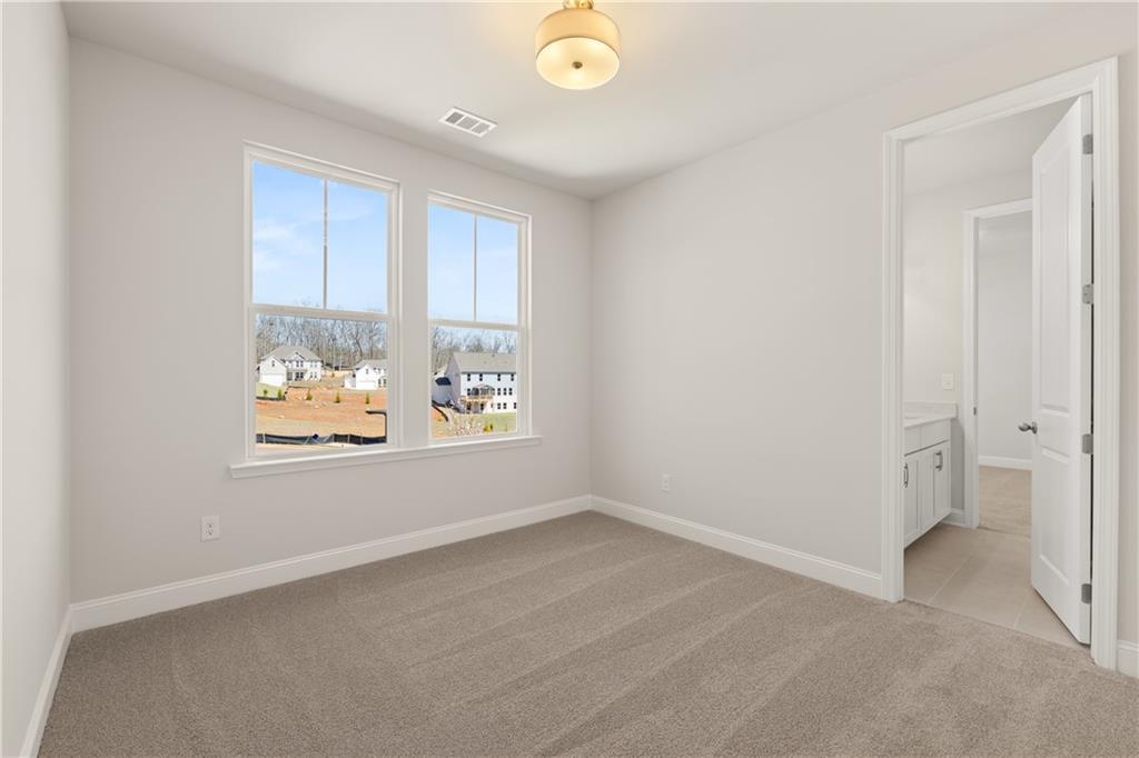 Bright bedroom with beige carpet, large windows overlooking neighborhood, en-suite bath in The Danbury C, Buford GA