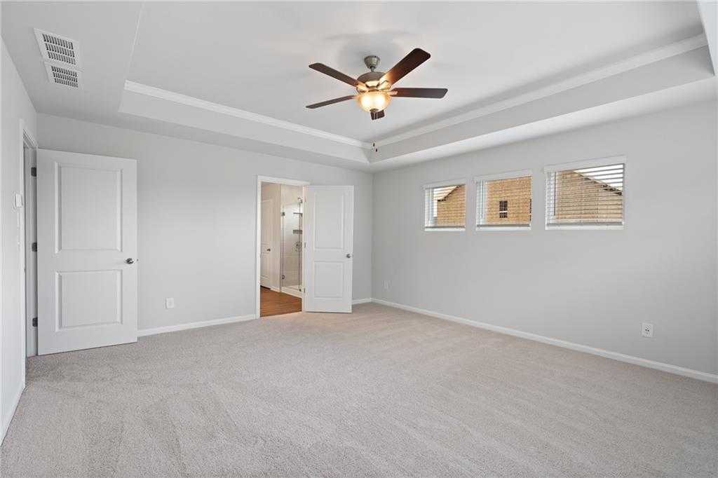 Spacious bedroom with ceiling fan, gray walls, open bathroom door in Davidson Homes The Hickory B, Winder, Georgia