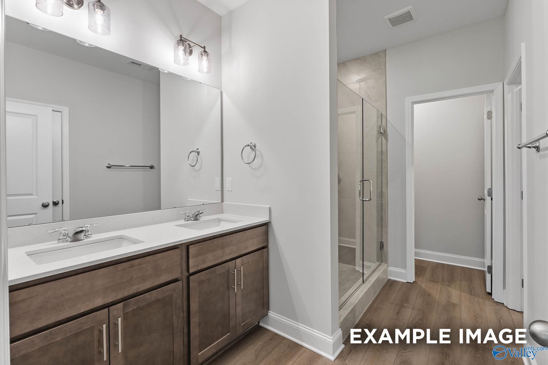 Elegant master bathroom with double sink vanity, frameless glass shower, and wood floors in Davidson Homes The Daphne C, Arab, Alabama