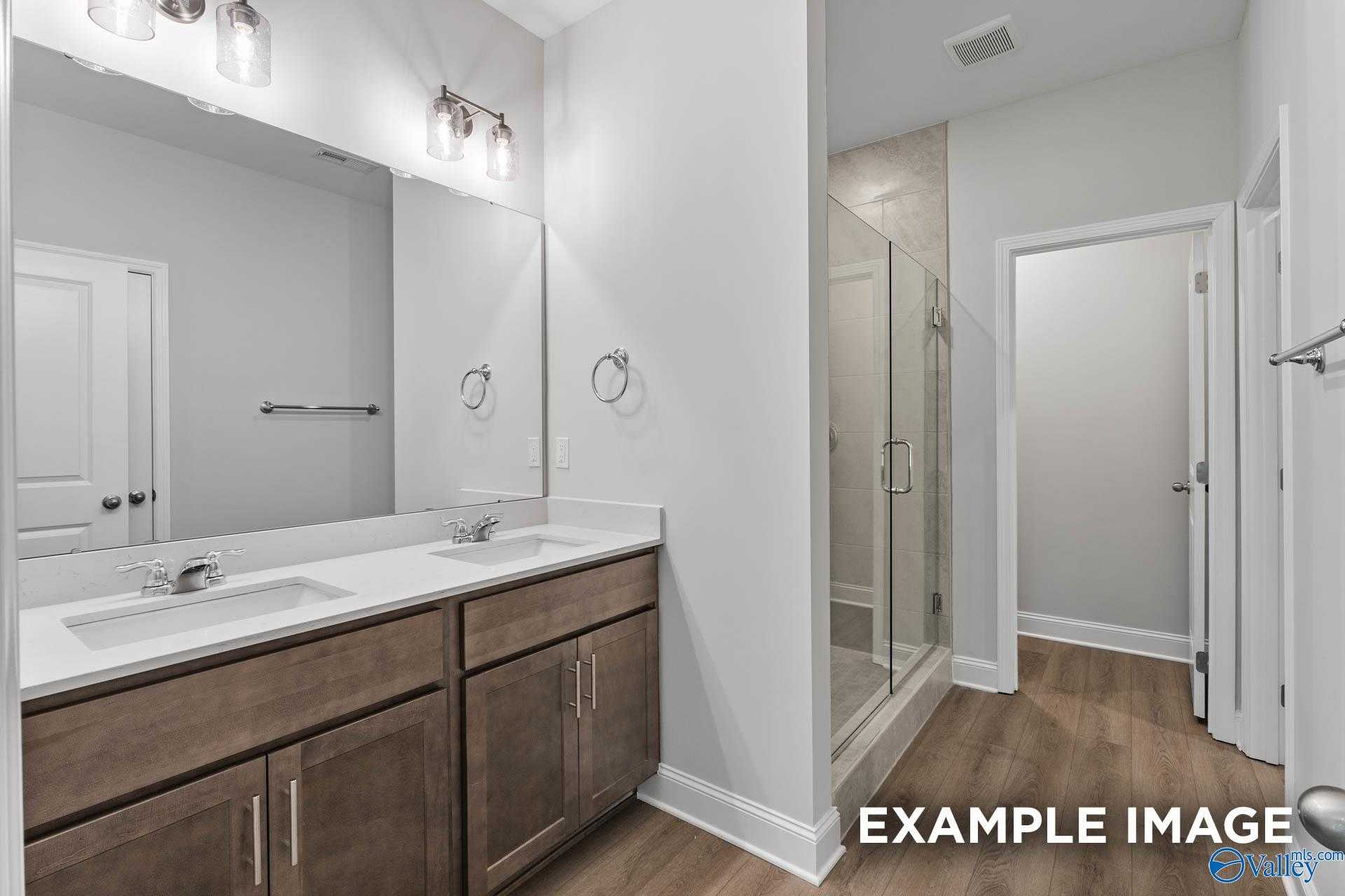 Elegant master bathroom with double sink vanity, frameless glass shower, and wood floors in Davidson Homes The Daphne C, Arab, Alabama