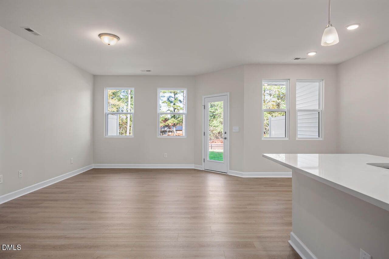 Bright open living area with white kitchen island, large windows, beige walls, and hardwood floors in Davidson Homes The Graham, Fuquay-Varina, NC