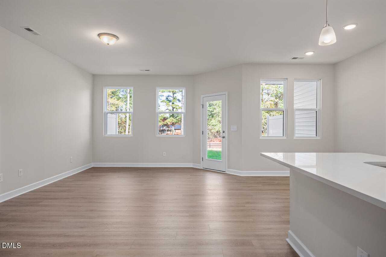 Bright open living area with white kitchen island, large windows, beige walls, and hardwood floors in Davidson Homes The Graham, Fuquay-Varina, NC