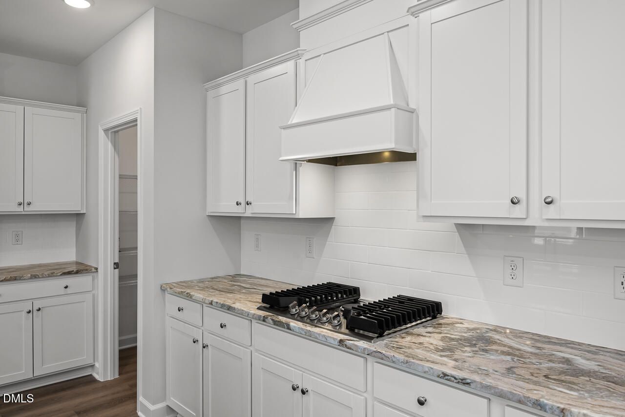 Modern kitchen with white cabinets, stone countertops, and gas cooktop in The Adalynn A floor plan at Gregory Village.