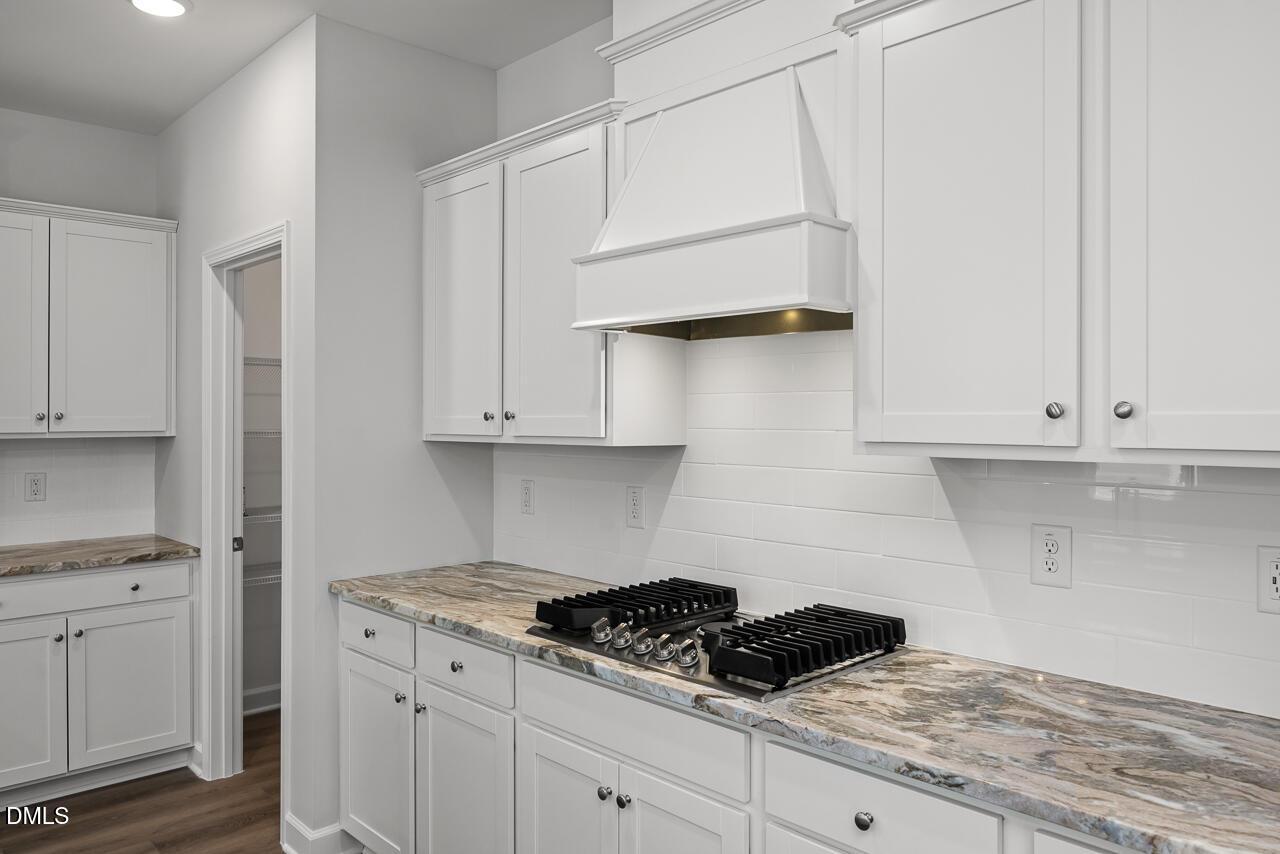 Modern kitchen with white cabinets, stone countertops, and gas cooktop in The Adalynn A floor plan at Gregory Village.