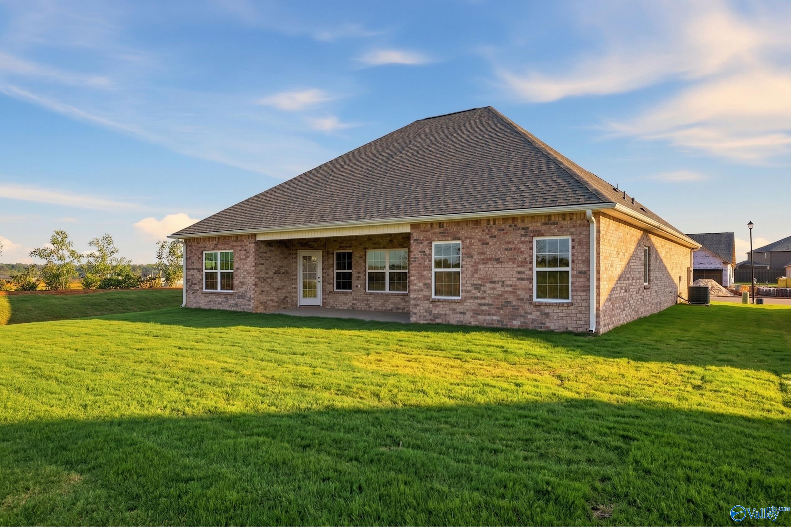 Brick ranch home exterior with gabled roof, covered patio, large windows, and lush green yard in Creekside, Harvest, Alabama