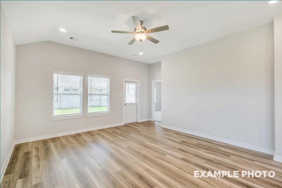 Bright living room with ceiling fan, large windows overlooking lawn, and luxury vinyl plank flooring in Davidson Homes The Riviera C, Dayton Texas