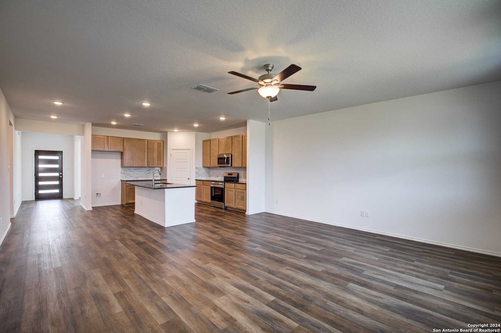 Modern open-concept kitchen with white cabinets, granite island, stainless appliances, and wood flooring in Davidson Homes The Douglas D, Seguin, Texas