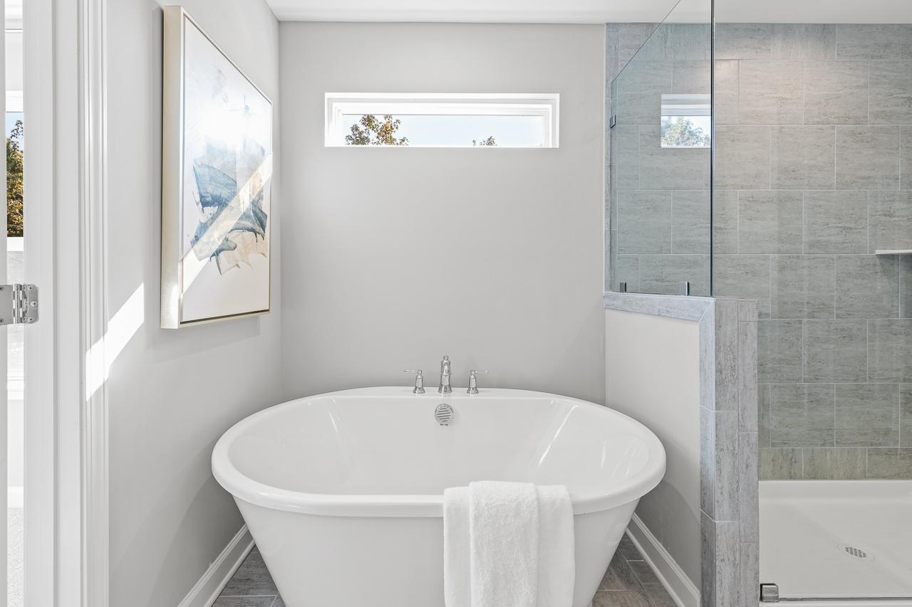 Luxurious master bathroom in The Hemlock featuring a freestanding soaking tub and modern glass-enclosed tile shower.