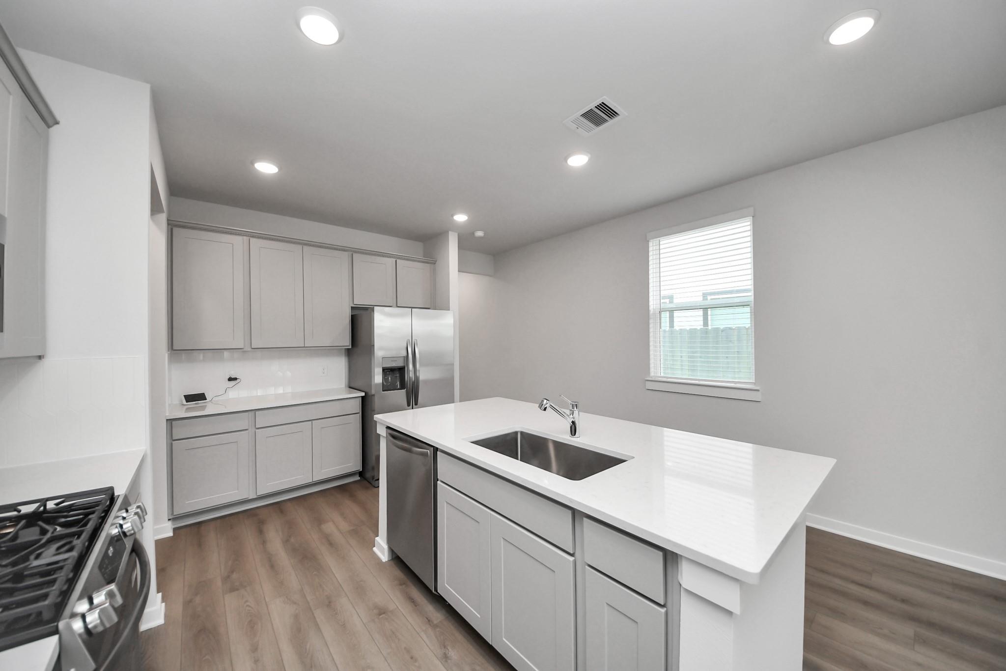 Modern kitchen with white island, quartz countertops, and stainless steel appliances in Davidson Homes The Frio F, Houston, Texas