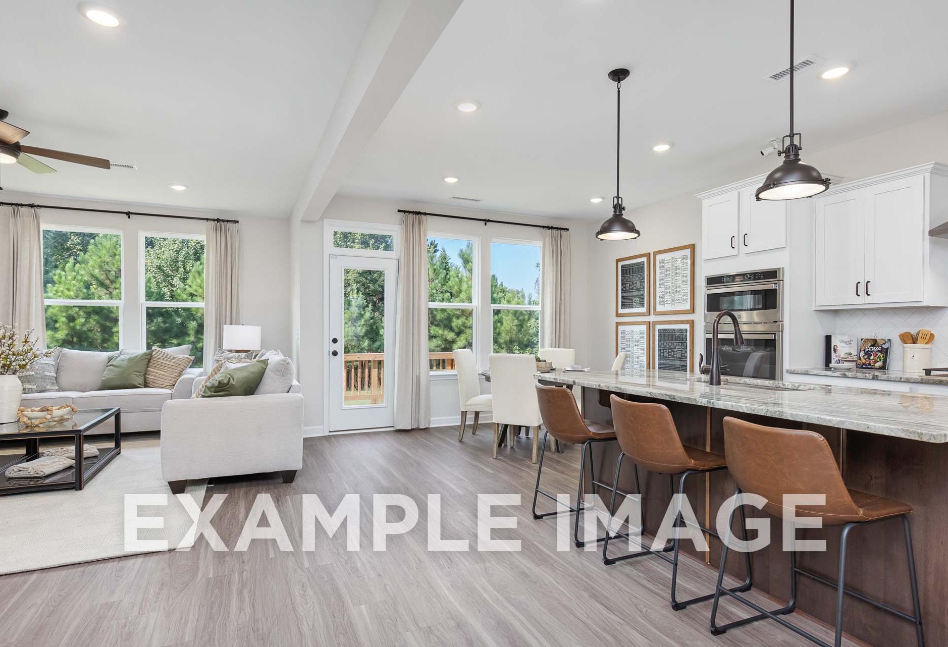 Open-concept kitchen and living area in The Willow E home with white cabinets, quartz island, bar stools, and large windows