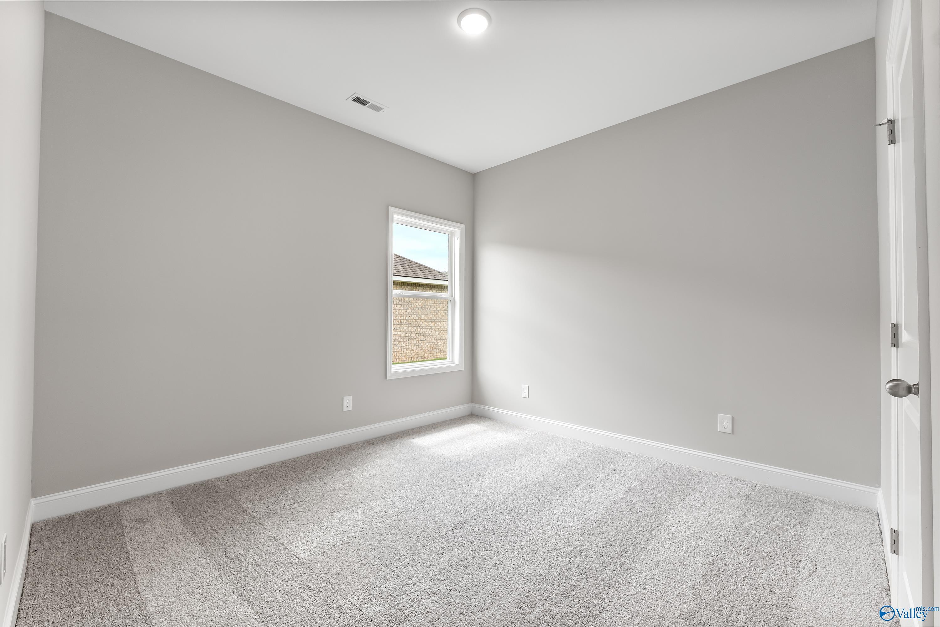 Bright secondary bedroom with light gray walls, large window, and carpeted floor in Davidson Homes The Franklin C, Huntsville AL
