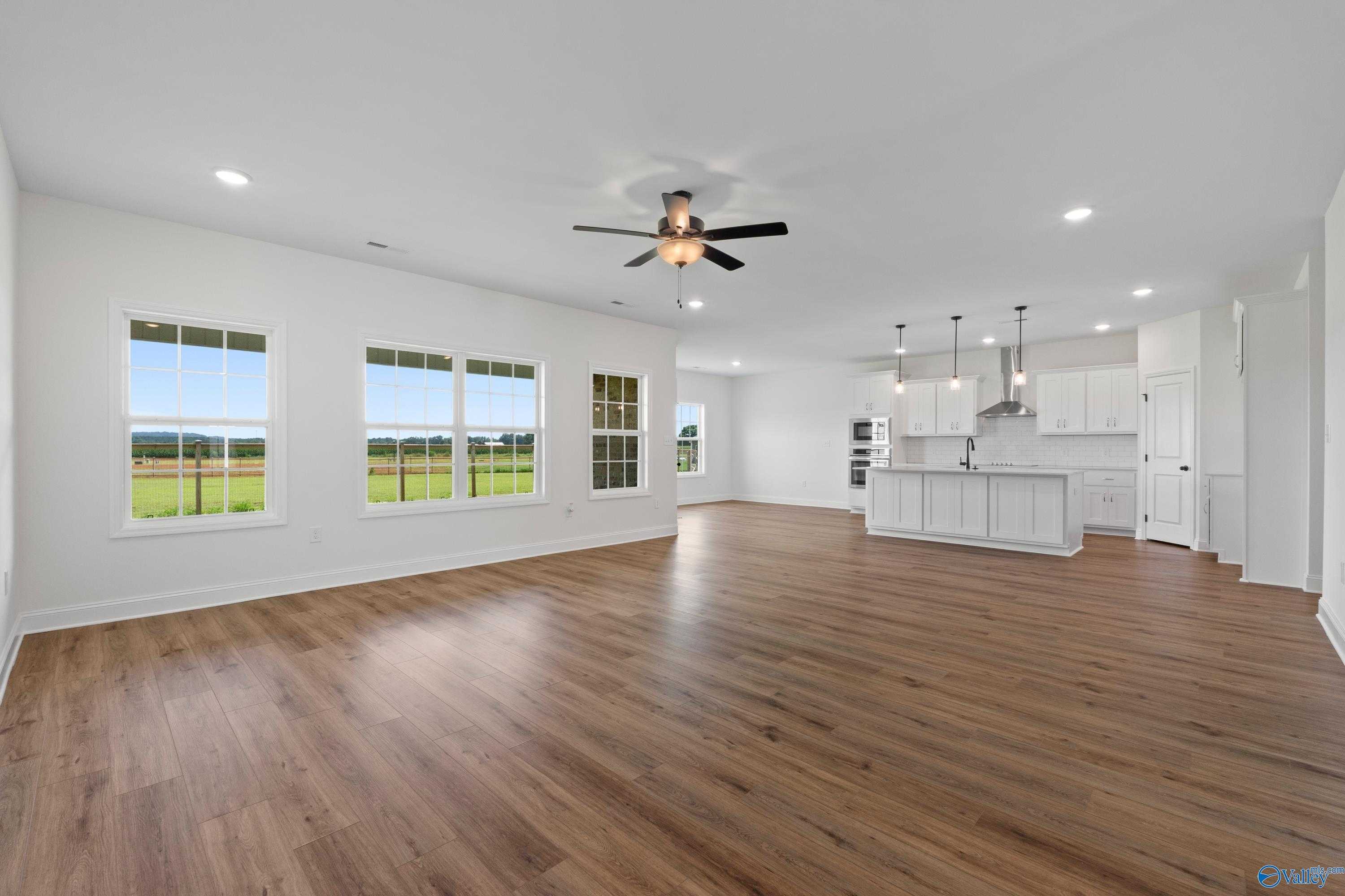 Open-concept living room and kitchen with hardwood floors, large windows overlooking fields in The Rockford B, Toney, Alabama