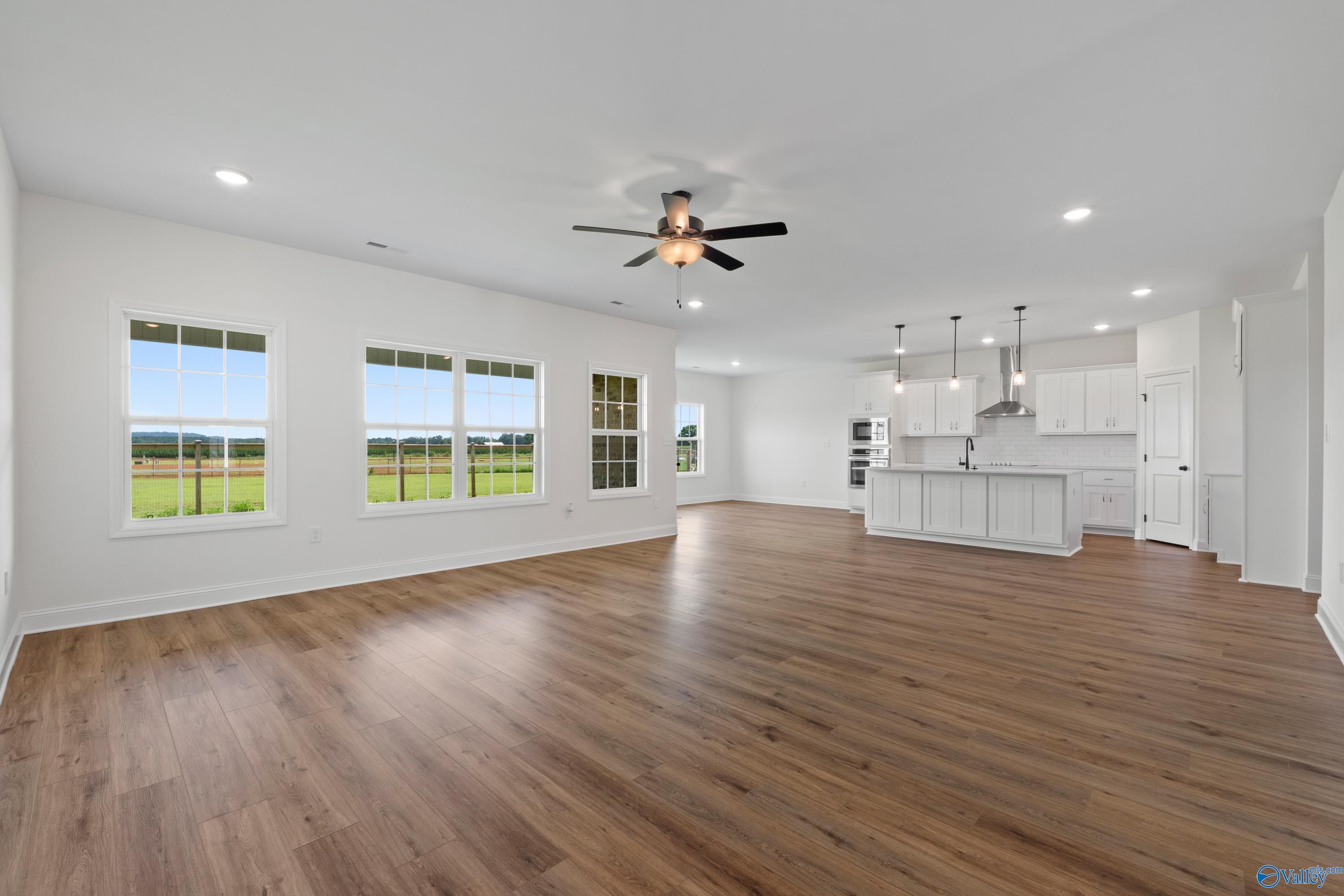 Bright open-concept living room with modern white kitchen island, hardwood floors, and large windows overlooking fields in Davidson Homes Rockford B, Toney, Alabama