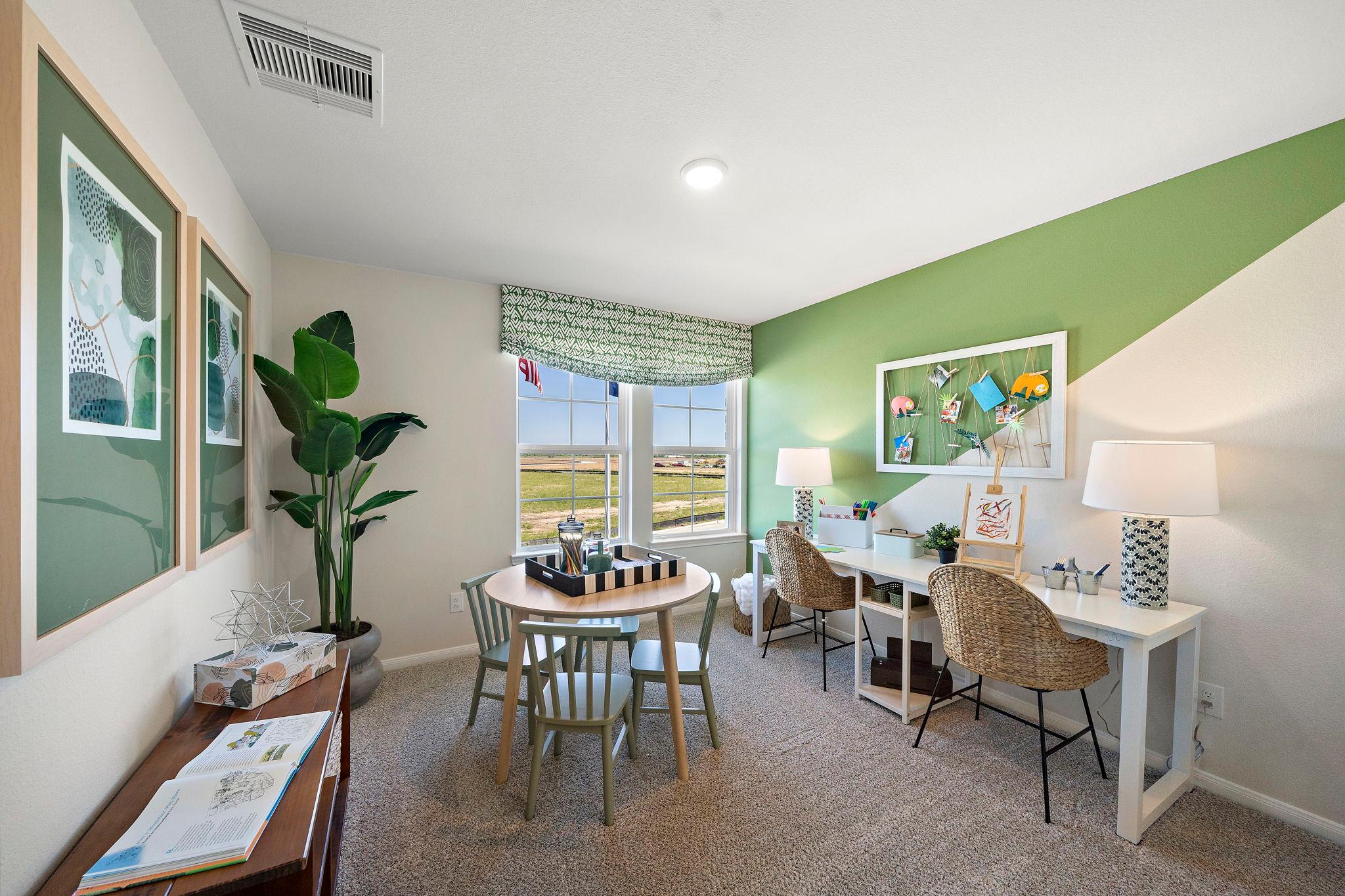 Bright study room in River Ranch Meadows Dayton TX featuring green accent wall, dual desks, round game table, potted plants, and field views