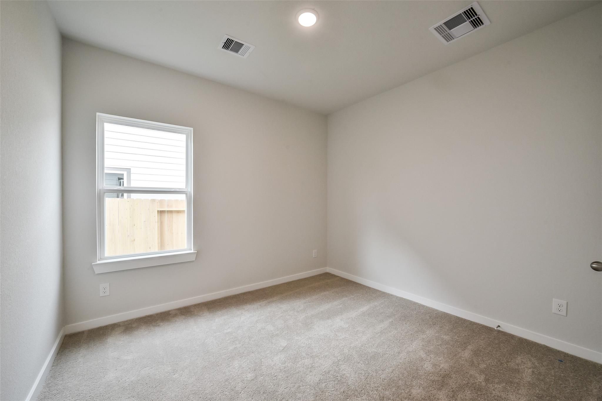 Spacious secondary bedroom with neutral walls, beige carpet, ceiling vents, and window overlooking fenced yard in The Frio F, Conroe, TX