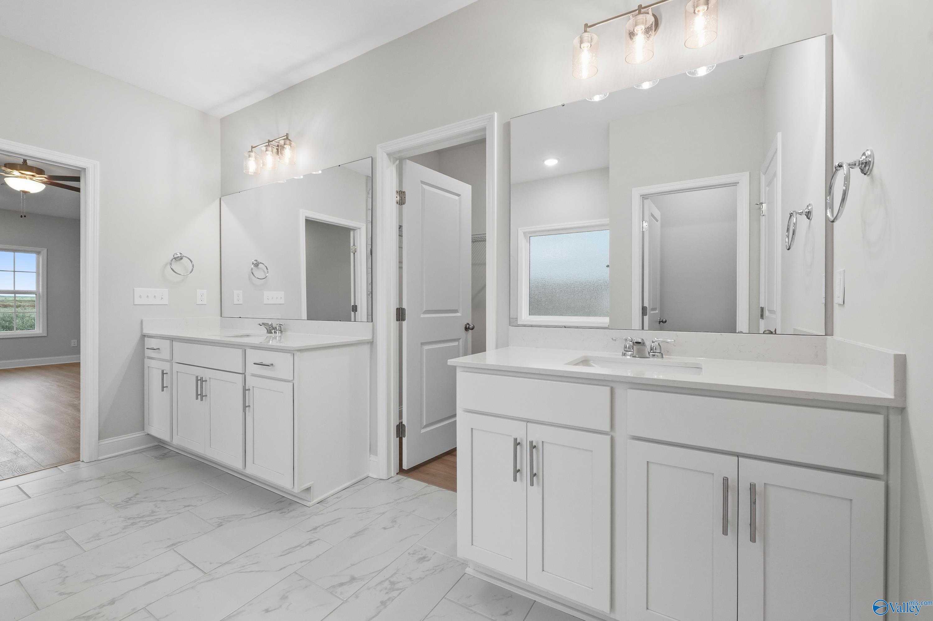 Modern master bathroom with double white vanity, large mirrors, and gray tile floor in Davidson Homes The Lanier, Harvest, AL
