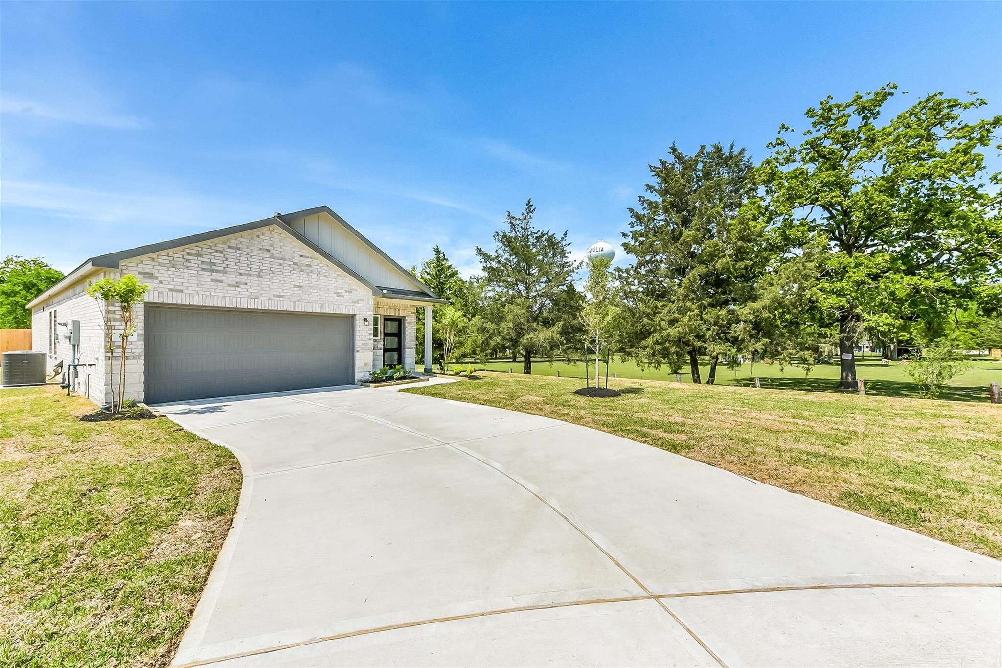 Modern white brick 1-story home with 2-car garage, curved driveway, palm tree, and lush trees in Windmill Estates, Magnolia, Texas by Davidson Homes