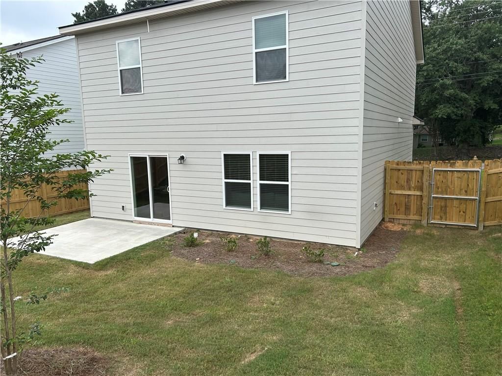 Two-story gray-sided home rear with sliding glass doors to covered patio, fenced grassy backyard in Phenix City, Alabama