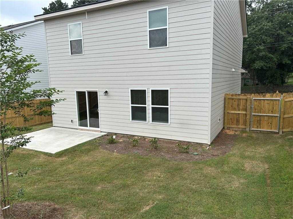 Two-story gray-sided home rear with sliding glass doors to covered patio, fenced grassy backyard in Phenix City, Alabama