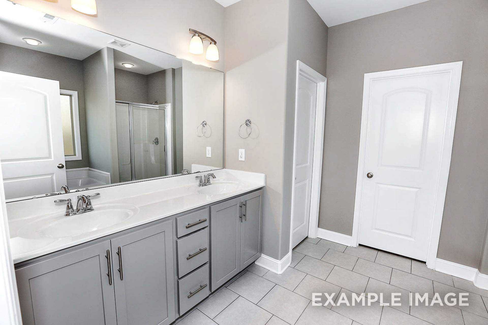 Modern master bathroom in The Montgomery B featuring double vanity with gray cabinets, large mirror, walk-in shower, and tiled floor