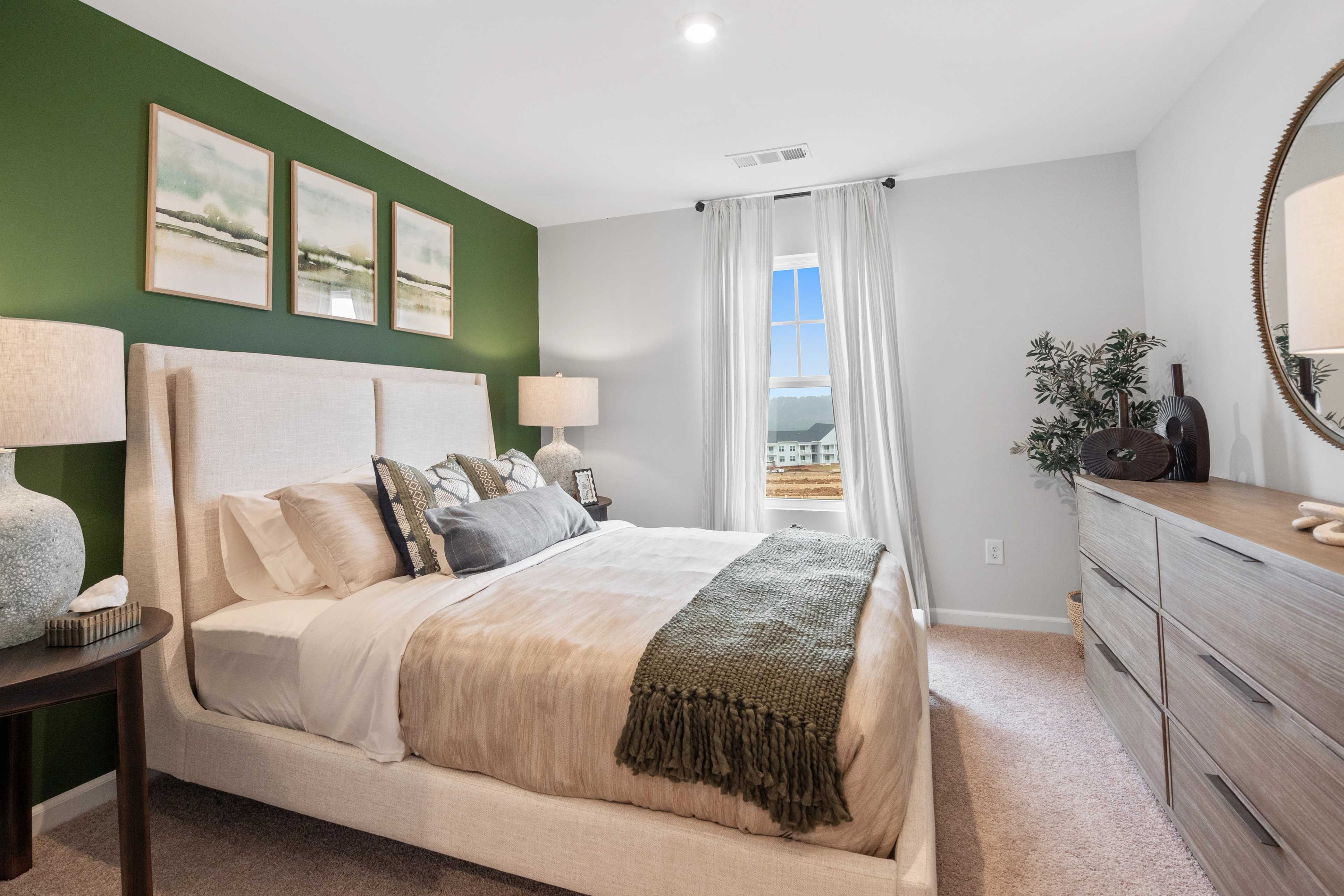 Cozy master bedroom with green accent wall, beige upholstered bed, and scenic window view at Stegall Village in Emerson, Georgia