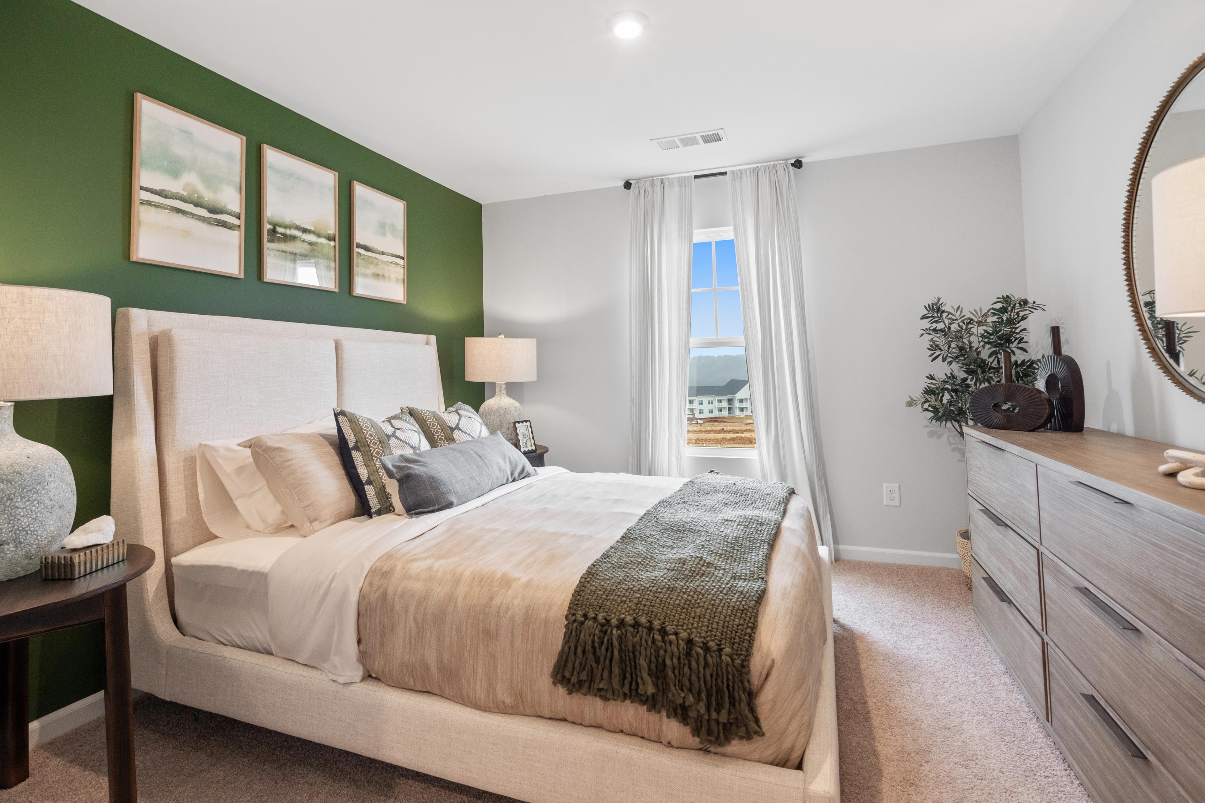 Cozy master bedroom with green accent wall, beige upholstered bed, and scenic window view at Stegall Village in Emerson, Georgia