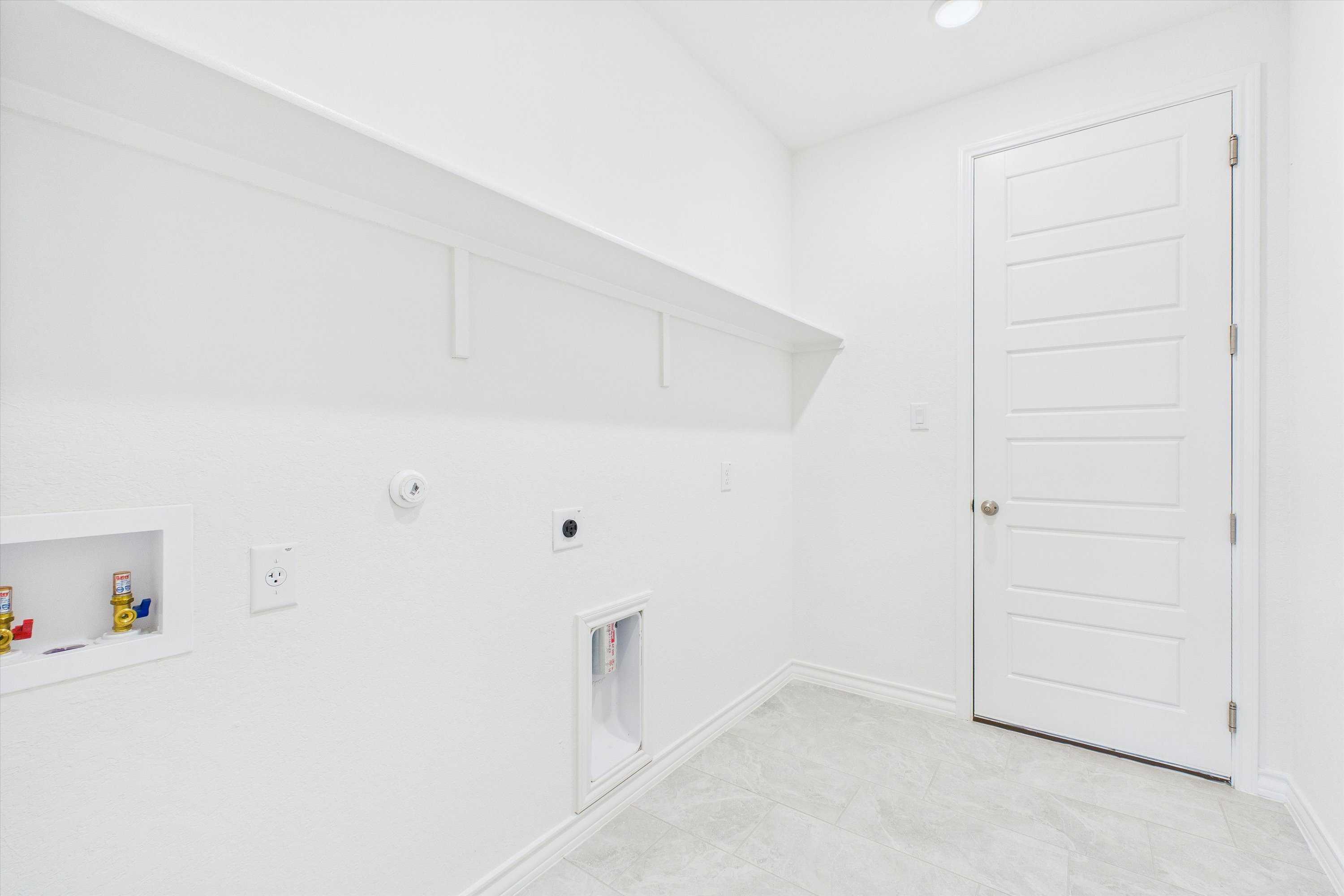 Bright white laundry room with built-in shelves, washer-dryer hookups in Davidson Homes Summerlin C, Castroville, Texas