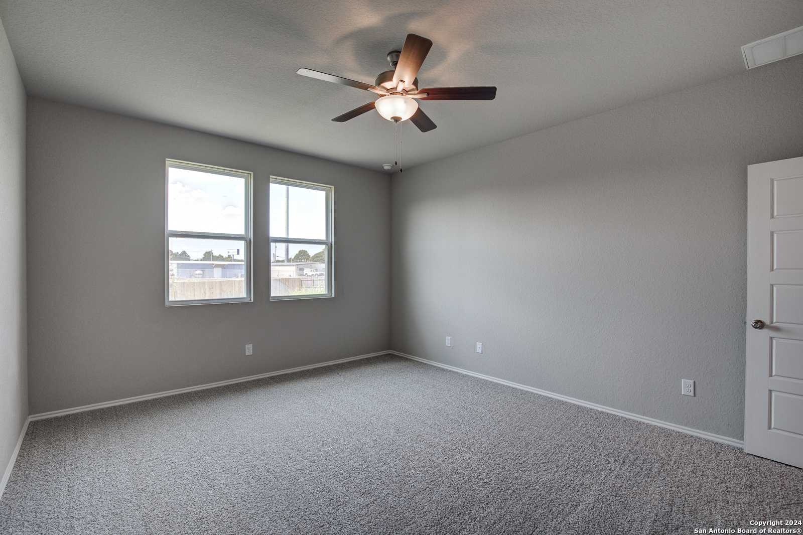 Spacious empty bedroom with gray walls, carpeted floor, ceiling fan, and dual windows in Davidson Homes The Daphne J, Seguin, Texas