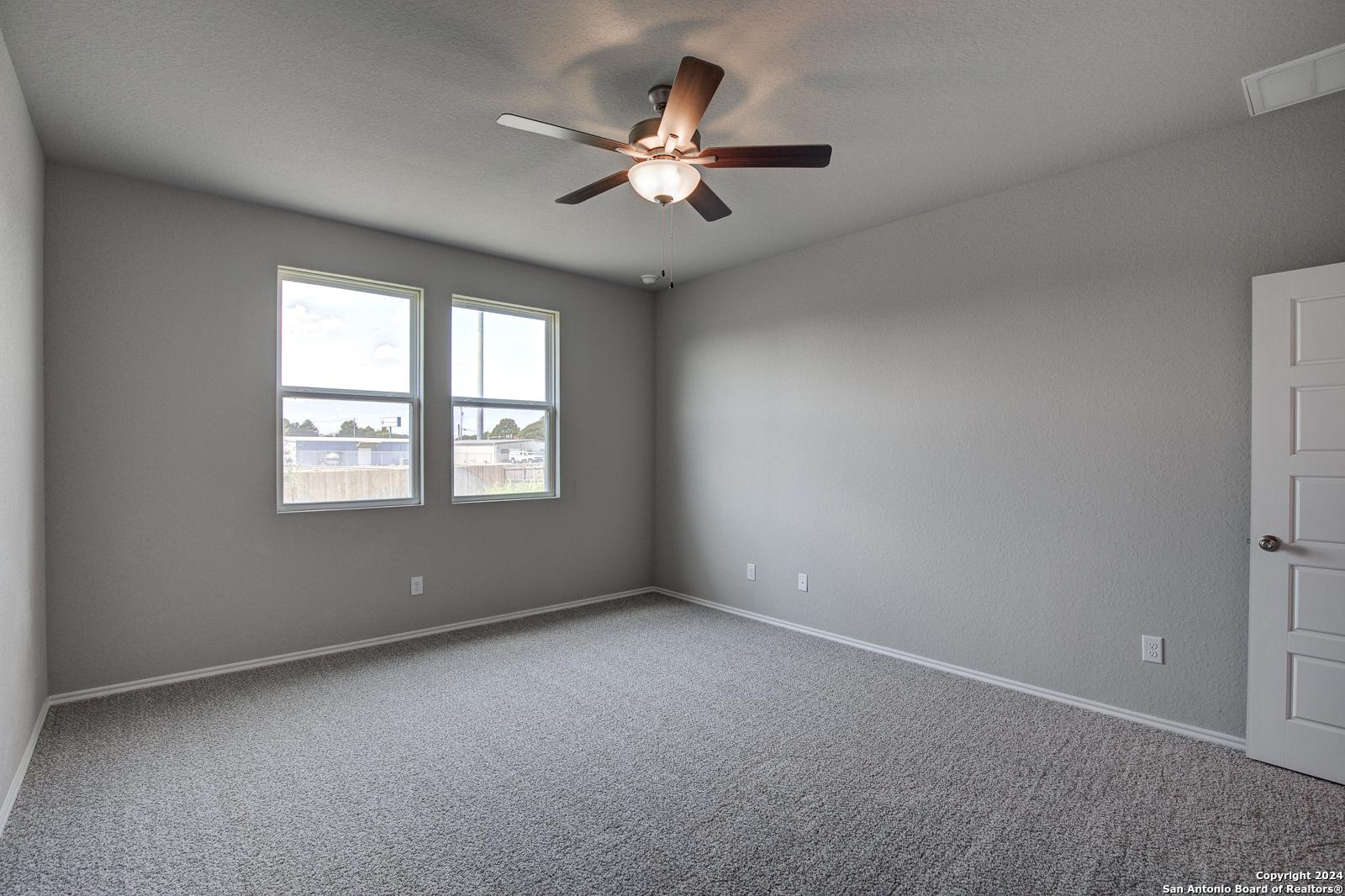 Spacious empty bedroom with gray walls, carpeted floor, ceiling fan, and dual windows in Davidson Homes The Daphne J, Seguin, Texas