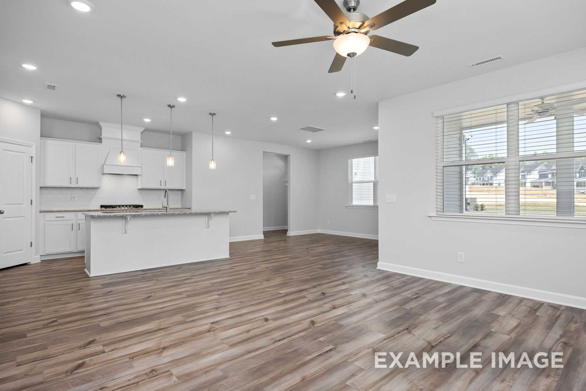 Open-concept kitchen in The Preston B featuring white island, cabinetry, hardwood floors, pendant lights, and large windows