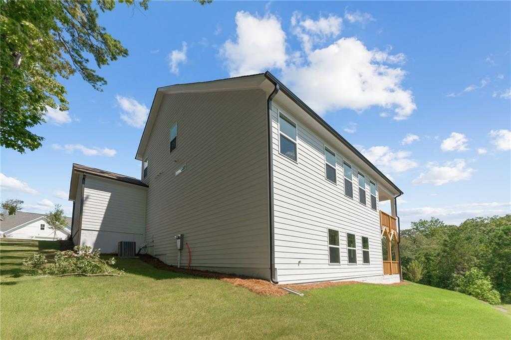 Side view of modern 1-story Davidson Homes The Ash B with unfinished basement, white siding, wooden deck, and green lawn in Riverwood, Dallas, Georgia