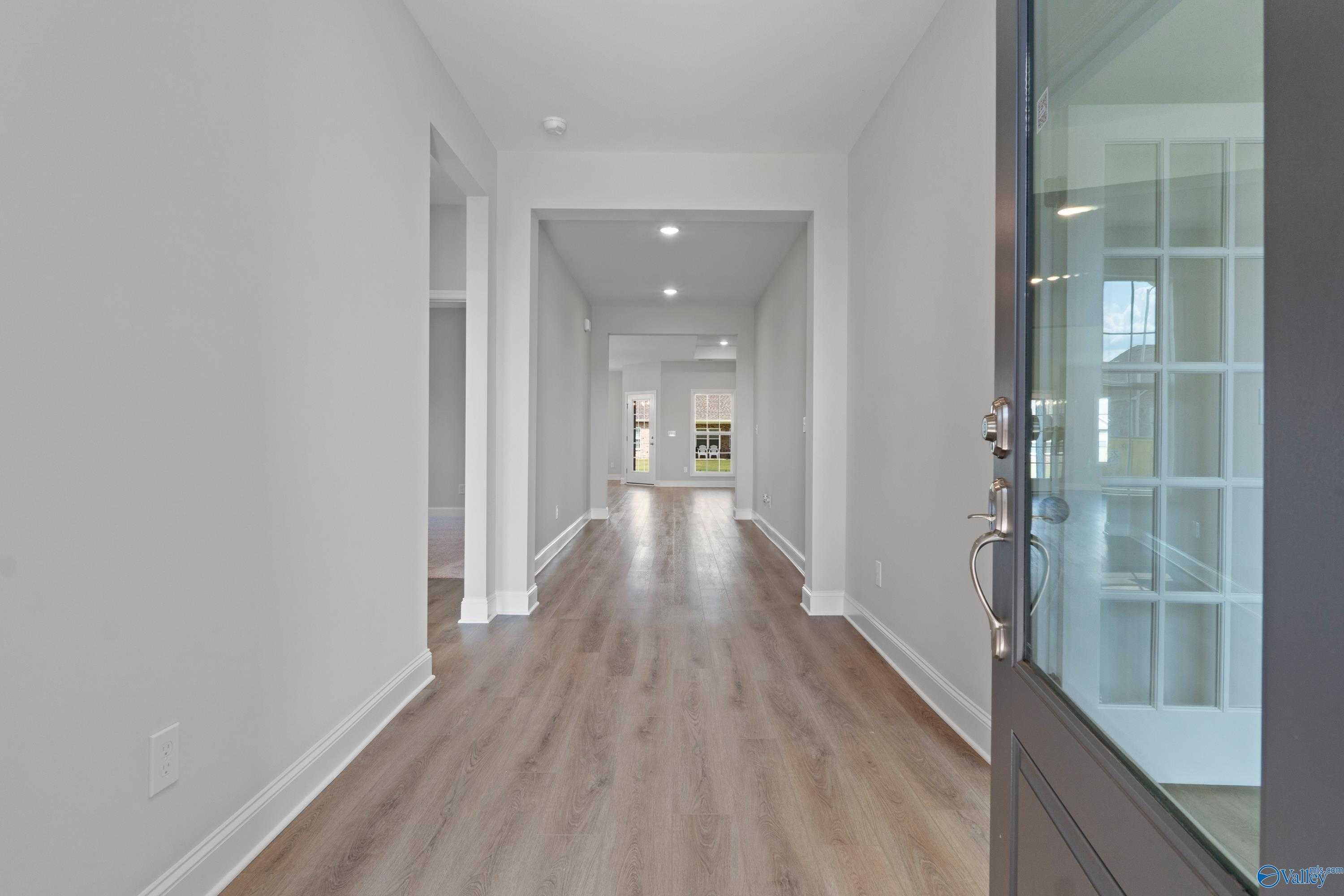 Elegant long hallway with light wood flooring, white walls, and recessed lighting in The Harrison B, Davidson Homes, Pikes Ridge, Meridianville, Alabama